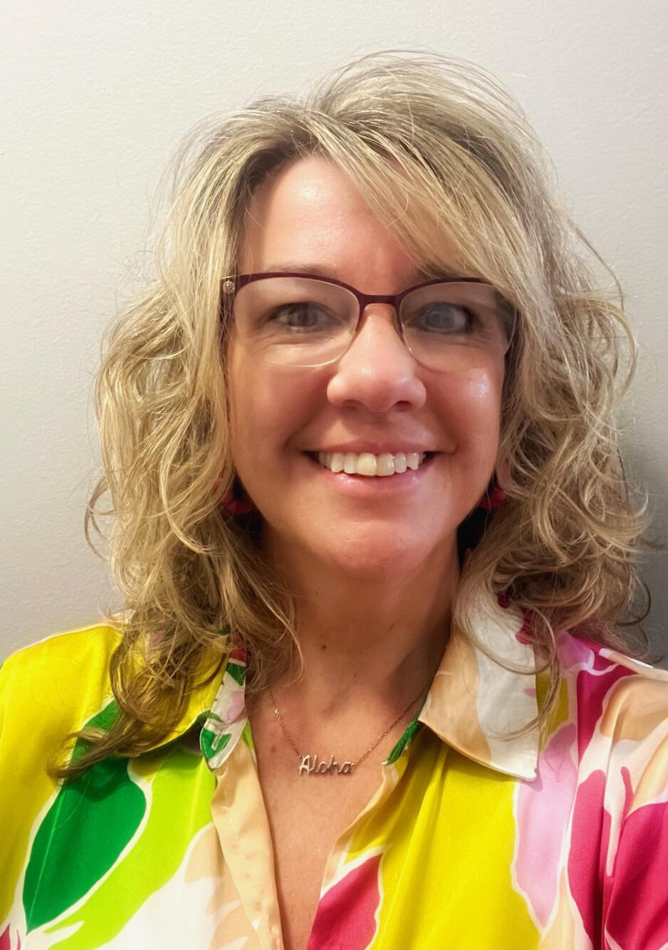 Kate Hydorn - Tutor in Ankeny, Iowa Kate a light skinned female with blonde curly hair wearing glasses standing in front of a wall with a tropical flowered shirt on.